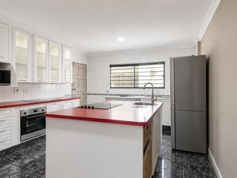 A functional kitchen featuring white cabinetry, a central island with a red countertop, built-in oven, hob, and tiled flooring.
