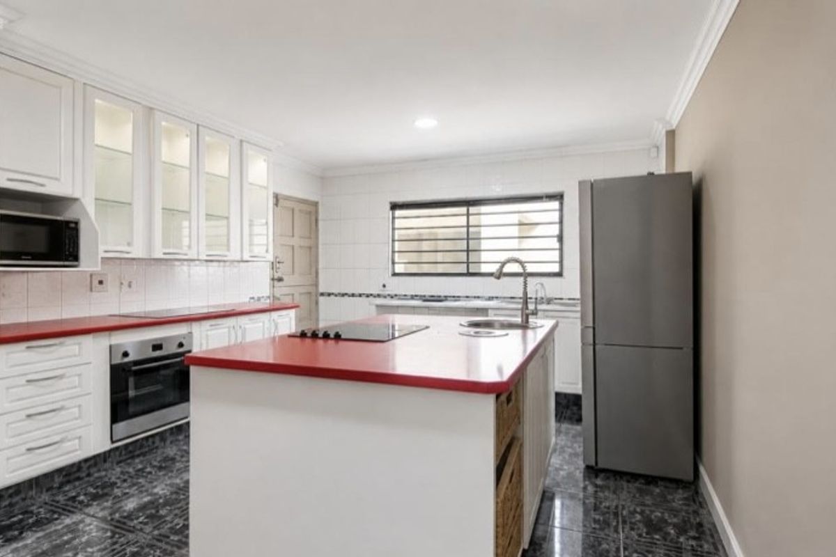 A functional kitchen featuring white cabinetry, a central island with a red countertop, built-in oven, hob, and tiled flooring.