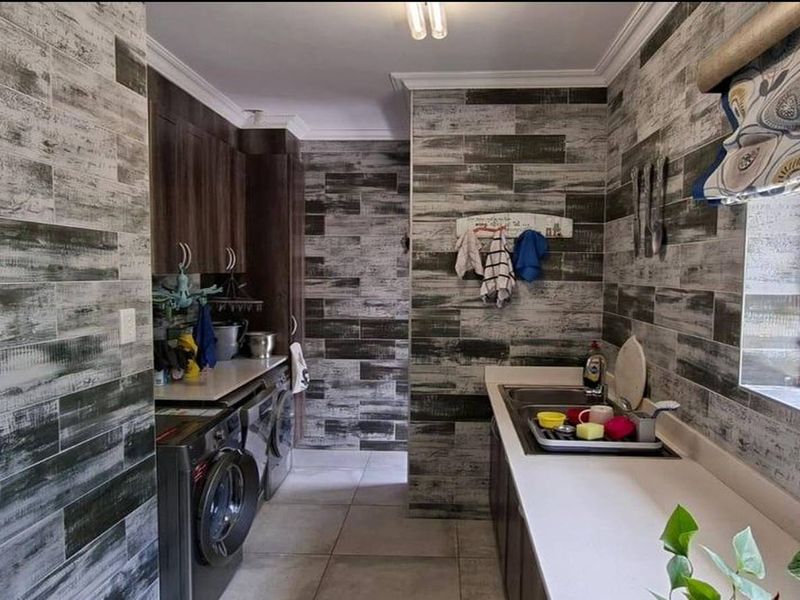 A functional laundry room featuring built-in cabinetry, a double sink, and modern wood-look tiled wall finishes.