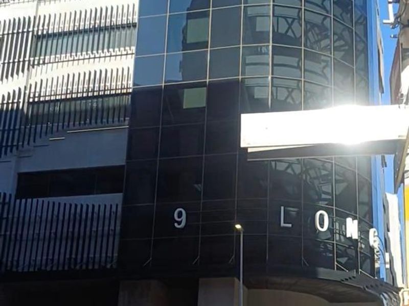 Modern multi-story office building facade featuring a prominent glass curtain wall and contemporary architectural cladding at the street level entrance.