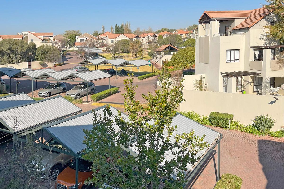 Elevated view of the apartment complex grounds, featuring paved driveways, covered parking structures, and landscaped garden areas.