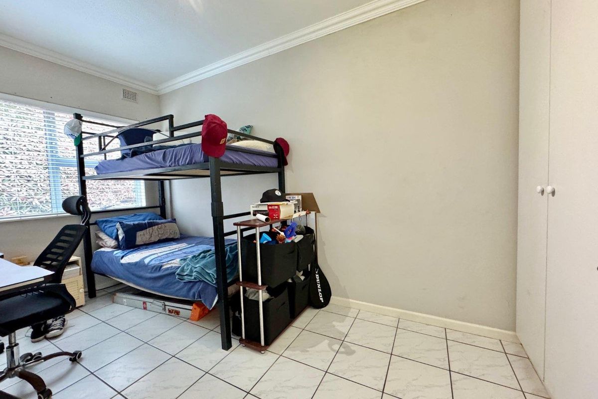 A bedroom featuring tiled flooring, built-in cupboards, and a window with security bars.