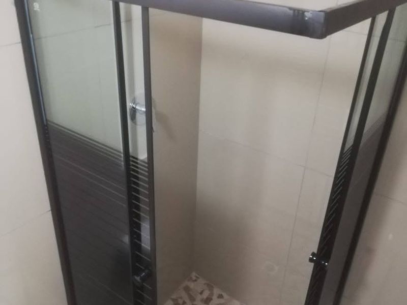 A clean bathroom shower stall featuring a modern black-framed glass enclosure, wall-mounted shower head, and decorative mosaic floor tiling.