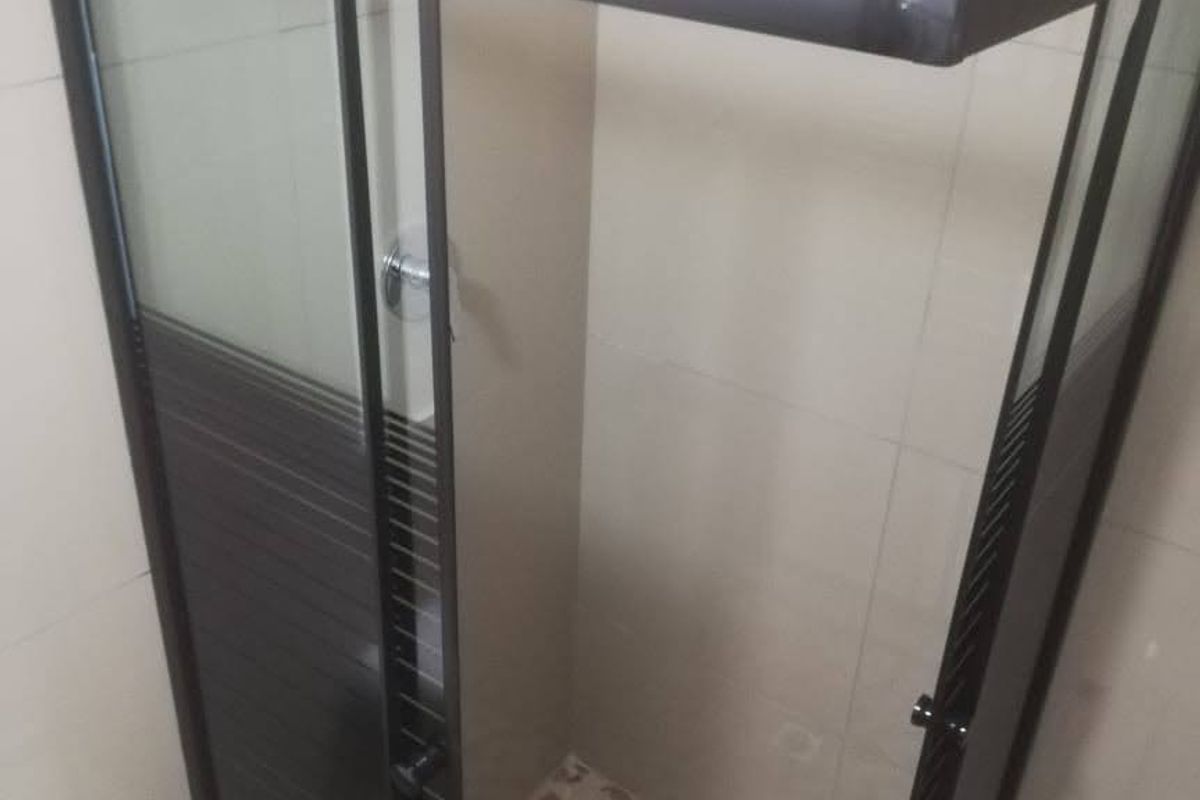A clean bathroom shower stall featuring a modern black-framed glass enclosure, wall-mounted shower head, and decorative mosaic floor tiling.