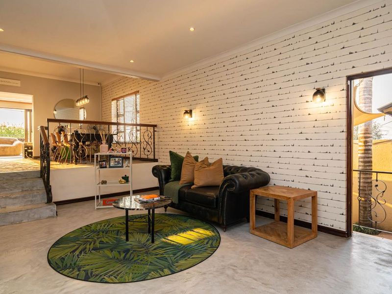 An open-plan living area featuring a split-level layout, decorative wall finishes, wrought iron balustrades, and direct access to an outdoor space.