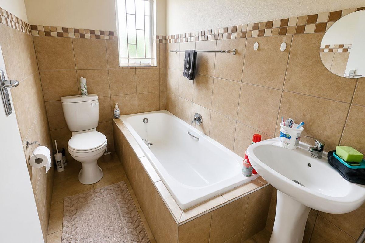 A functional bathroom featuring a built-in bathtub, pedestal basin, and toilet with neutral wall tiling and a window for natural light.
