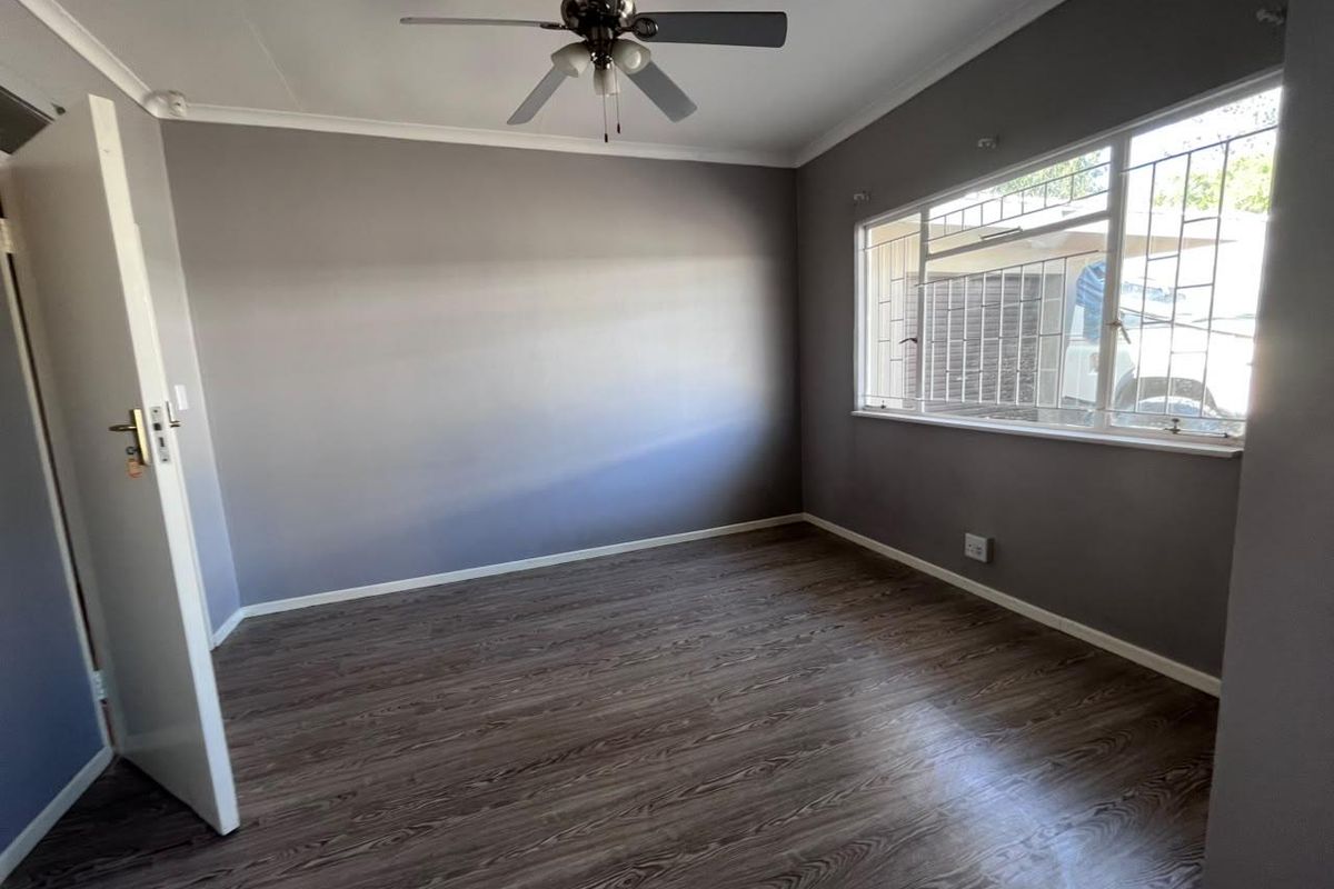 A clean, empty bedroom featuring modern laminate flooring, a ceiling fan, and security bars on the window.