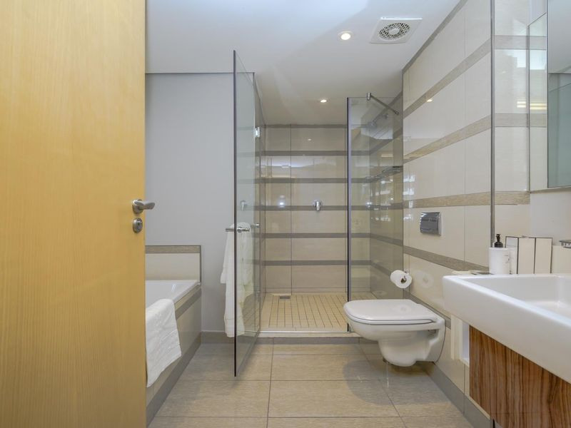 Modern bathroom featuring a wall-mounted toilet, glass-enclosed shower, built-in bathtub, and a vanity basin with neutral tiled finishes.
