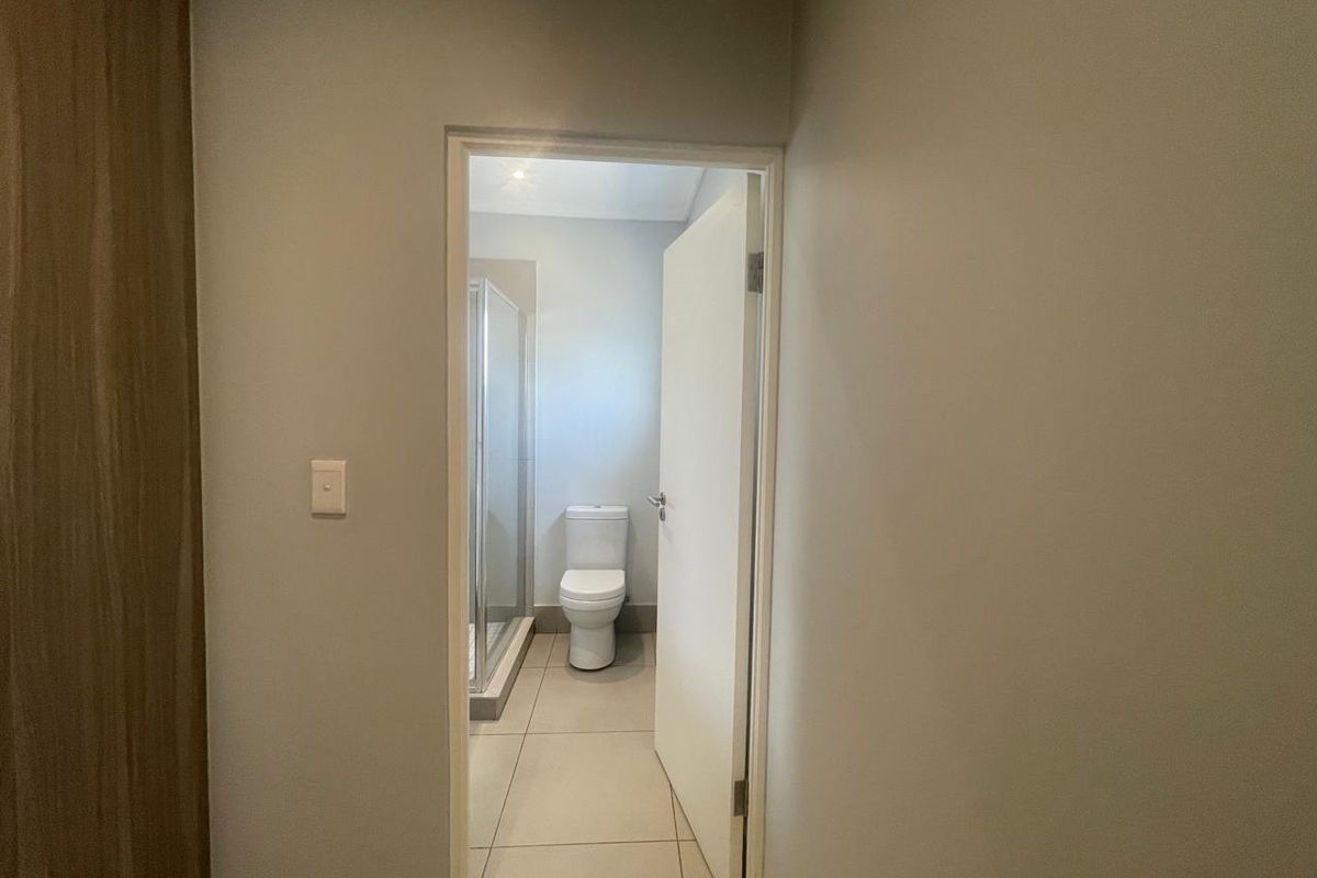 A view through a doorway into a clean, modern bathroom featuring a shower enclosure and a toilet with neutral tiled flooring.