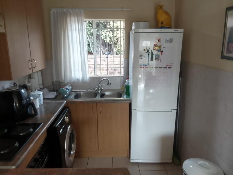 A functional kitchen featuring laminate cabinetry, a double sink with mixer tap, tiled splashback, and security bars on the window.