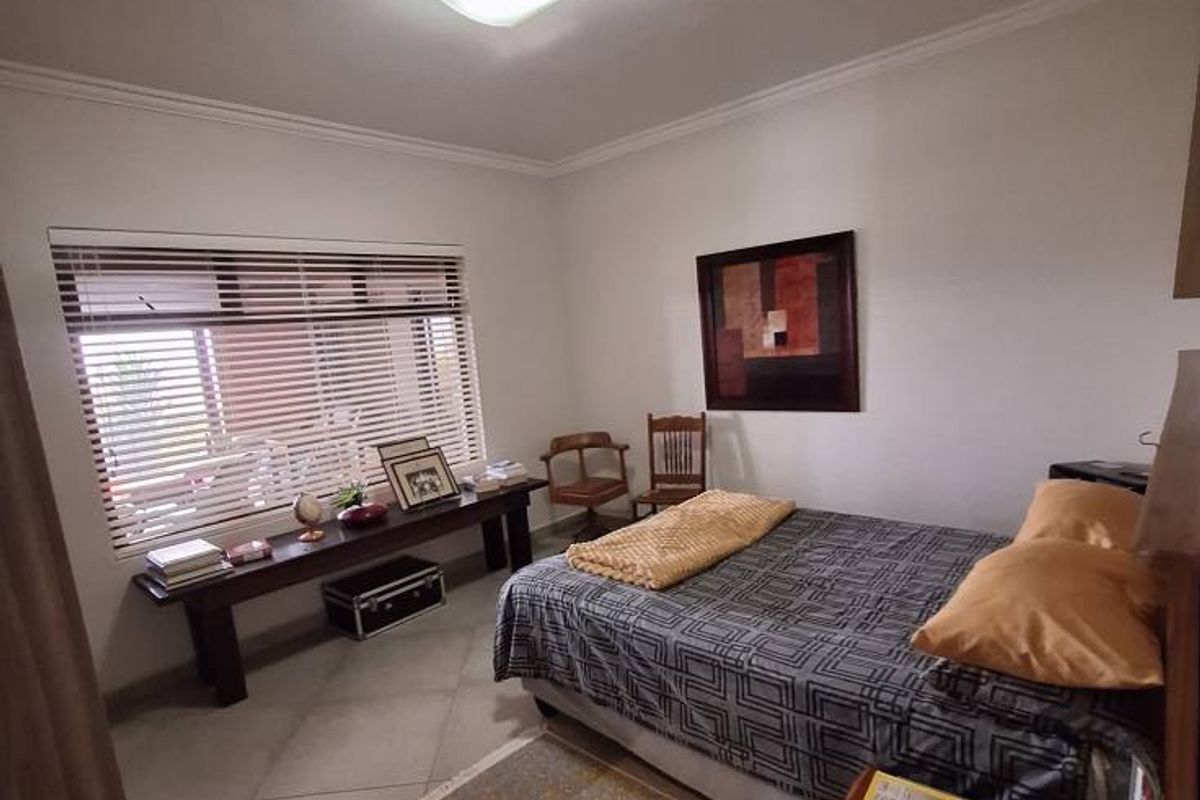 A well-lit bedroom featuring tiled flooring, a large window with horizontal blinds, and a central ceiling light fixture.