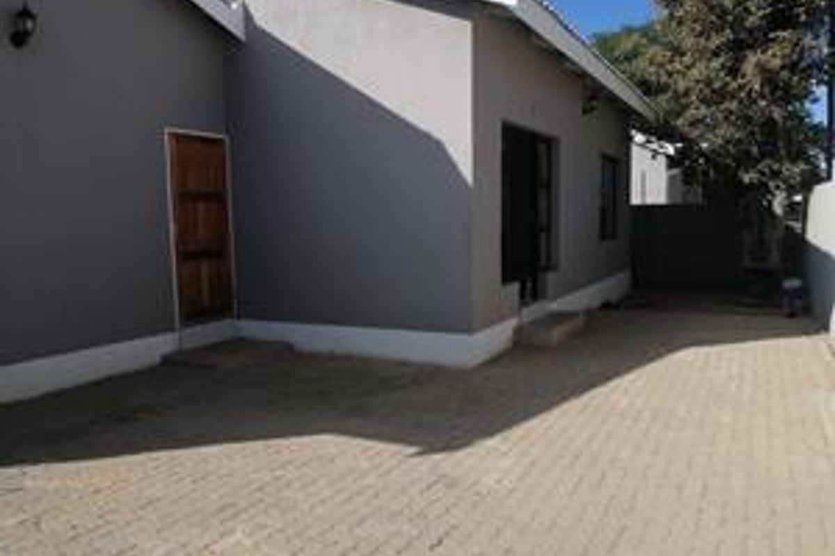 Rear exterior view of the townhouse featuring a paved courtyard area, grey painted walls, and access points to the main dwelling.