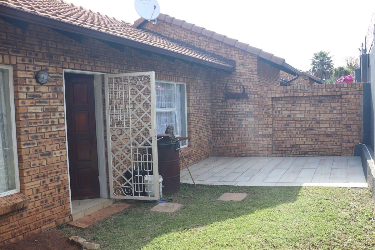 Rear view of the townhouse featuring a face brick exterior, tiled roof, a small paved patio area, and a private lawn.