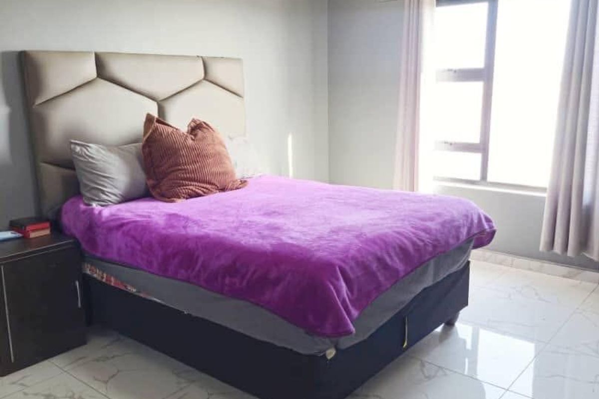 A well-lit bedroom featuring modern marble-look floor tiles, neutral grey walls, and a large window with curtain fixtures.