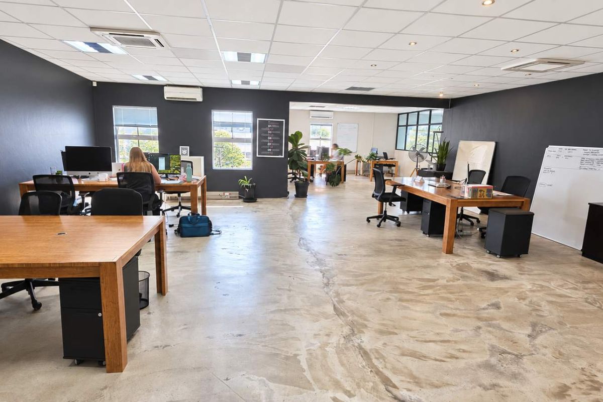 Spacious open-plan office area featuring polished concrete floors, suspended ceiling with recessed lighting, and integrated air conditioning units.