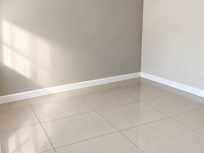 A clean, empty room featuring neutral painted walls, crown molding, white baseboards, and polished large-format porcelain floor tiles.