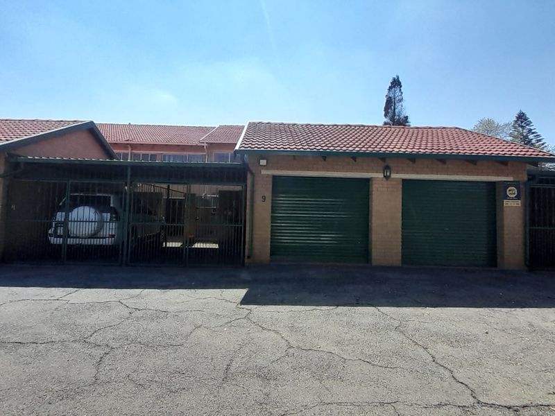 Front exterior view of the townhouse featuring a brick facade, tiled roof, and multiple secure garage bays with roller shutter doors.