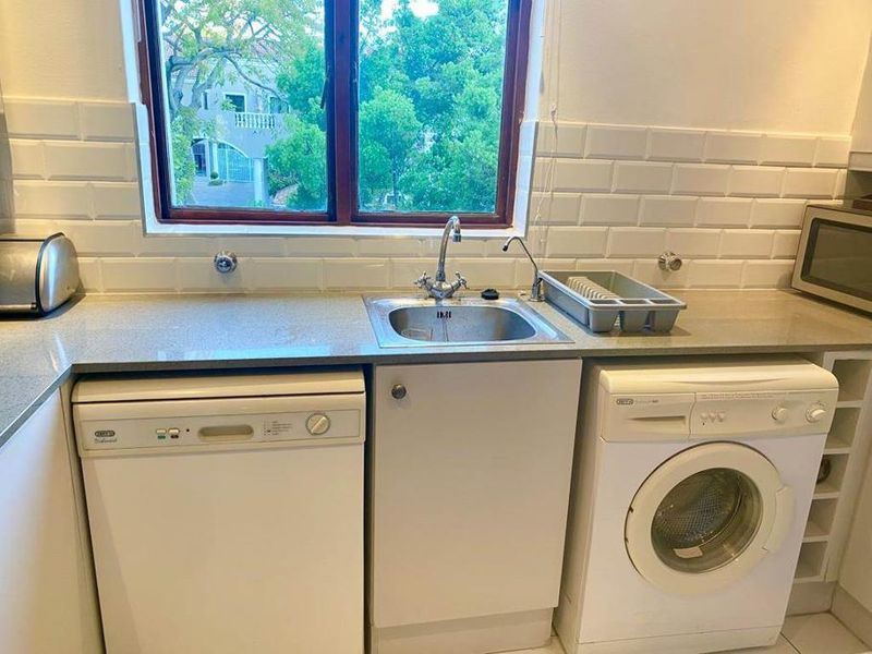 A functional kitchen area featuring a subway tile backsplash, stone countertops, a stainless steel sink, and integrated laundry and dishwashing appliances.