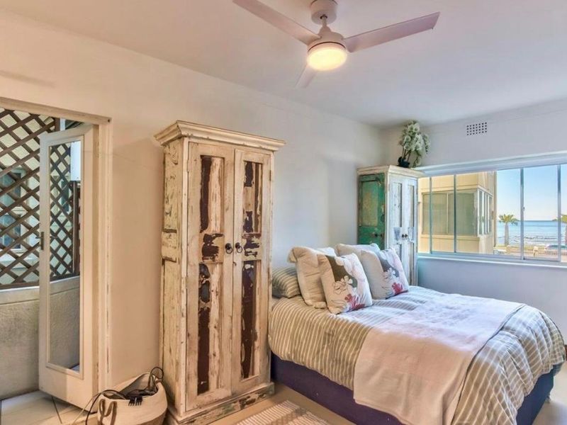 A bedroom featuring a ceiling fan, tiled flooring, and a window with a view of the ocean.