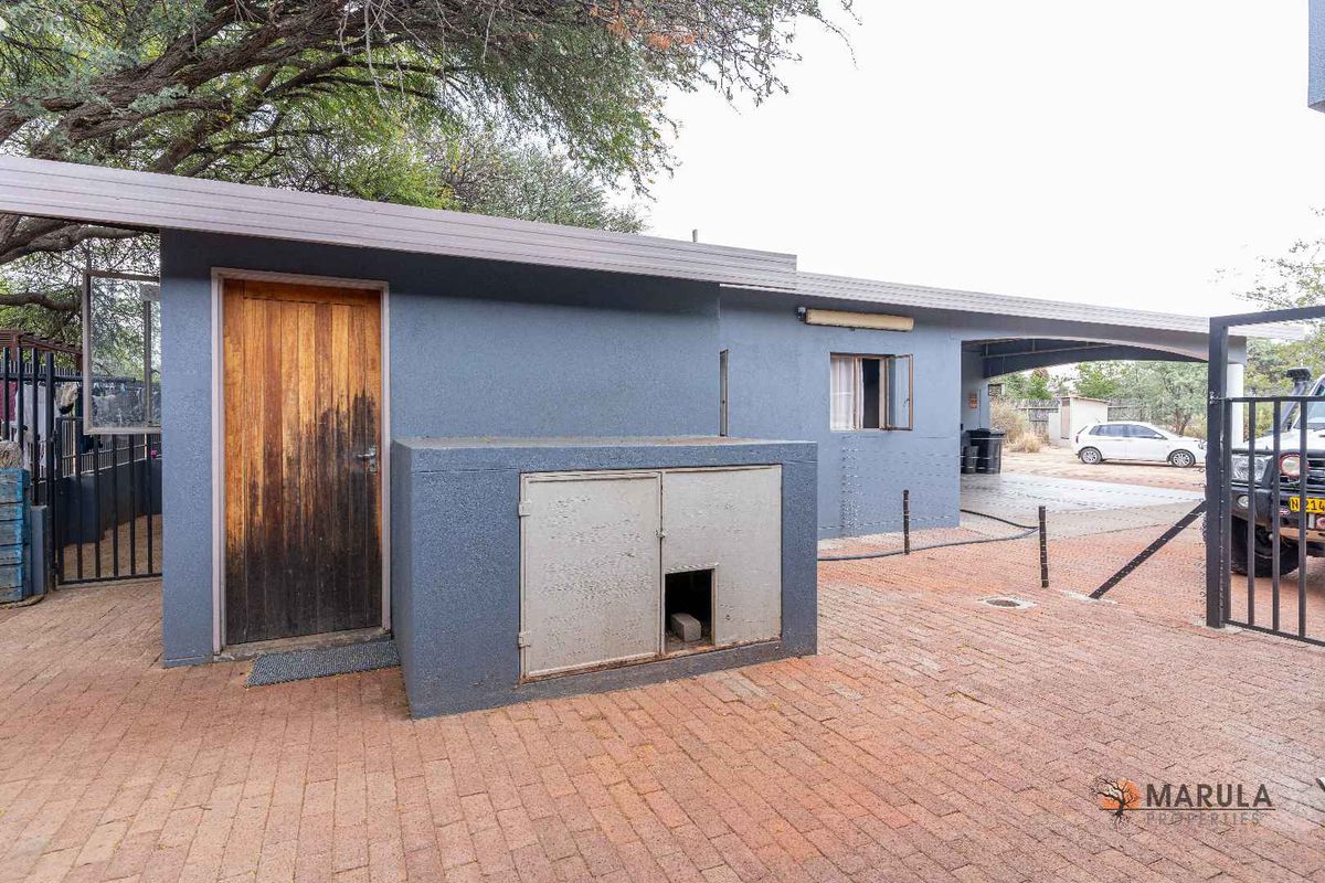 Exterior view of a paved courtyard area featuring a built-in outdoor storage unit, a wooden door, and a covered carport structure.