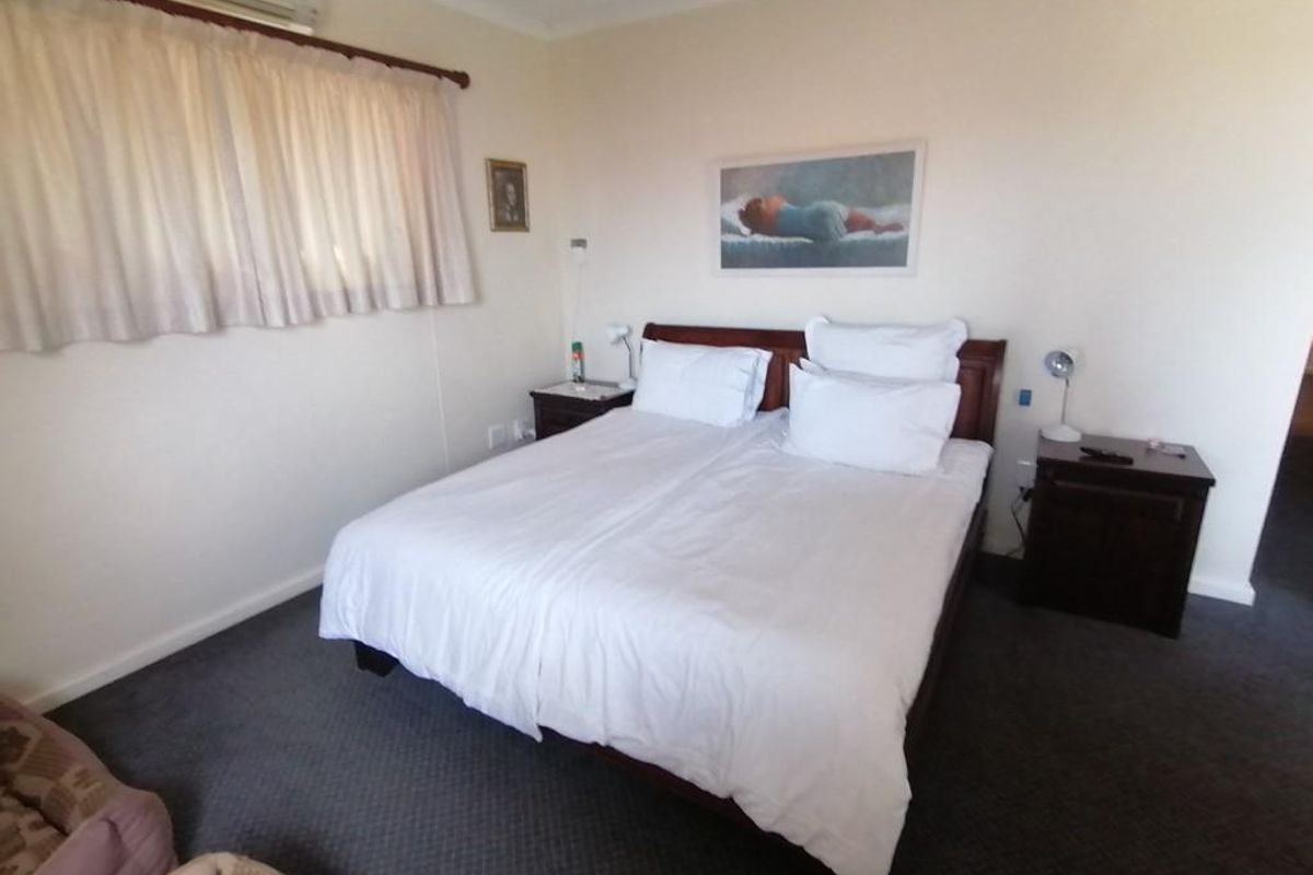 A well-lit bedroom featuring neutral walls, carpeted flooring, and a wall-mounted air conditioning unit.