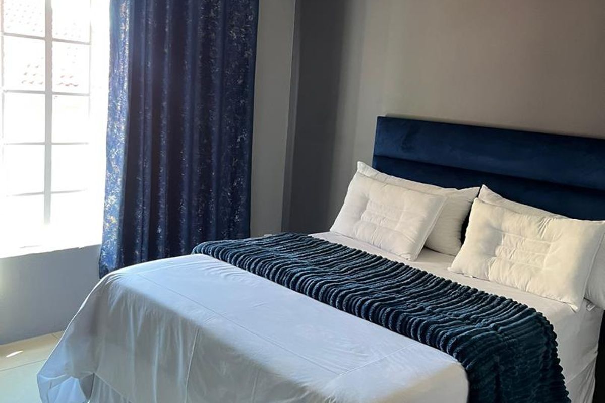 A well-maintained bedroom featuring tiled flooring, crown molding, and a large window allowing for natural light.