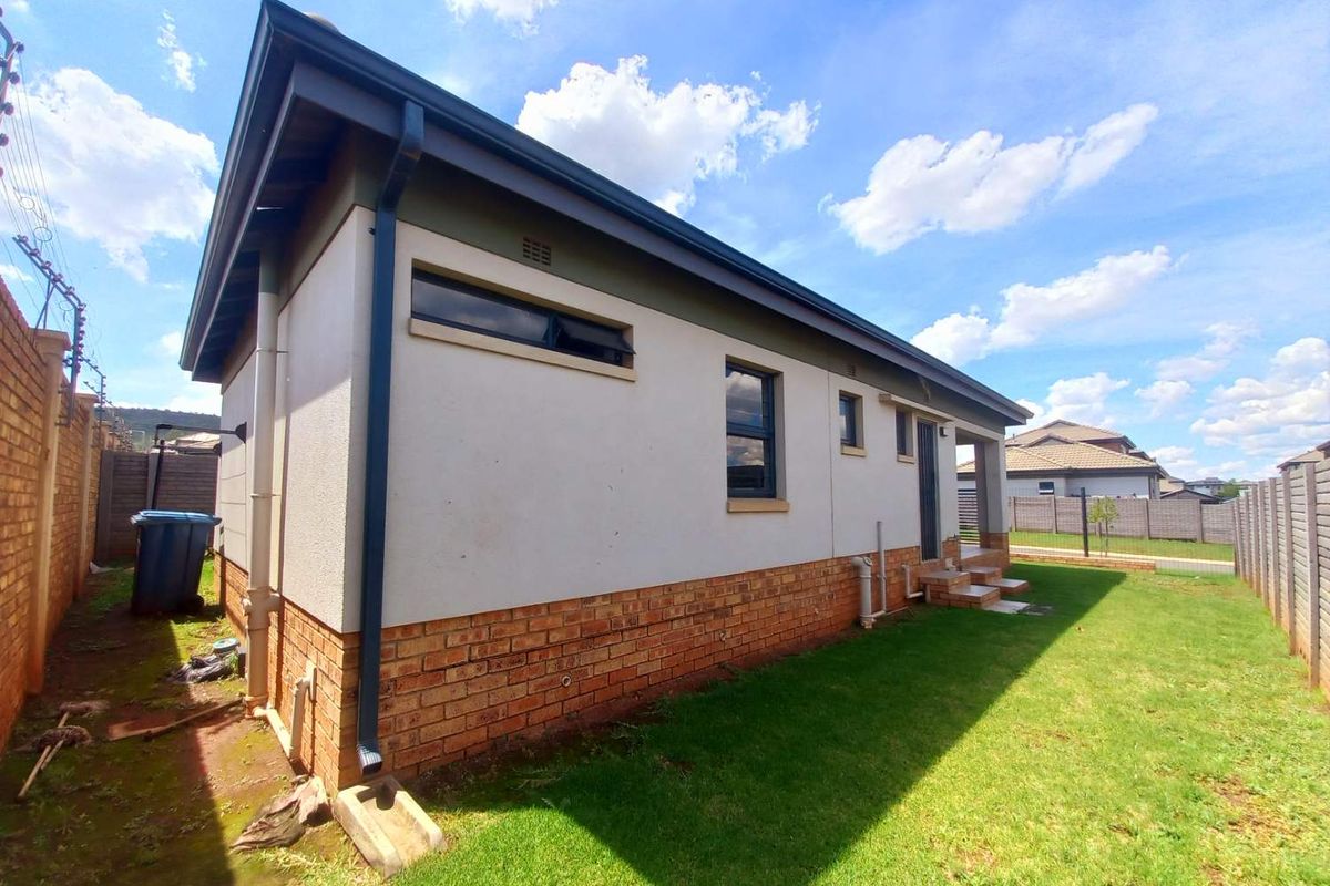 Side view of the house featuring a brick base, plastered upper walls, dark window frames, and a well-maintained lawn area.