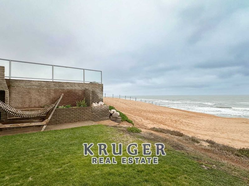 Outdoor patio area featuring a built-in braai, glass balustrade, and direct access to the beach, offering expansive ocean views.