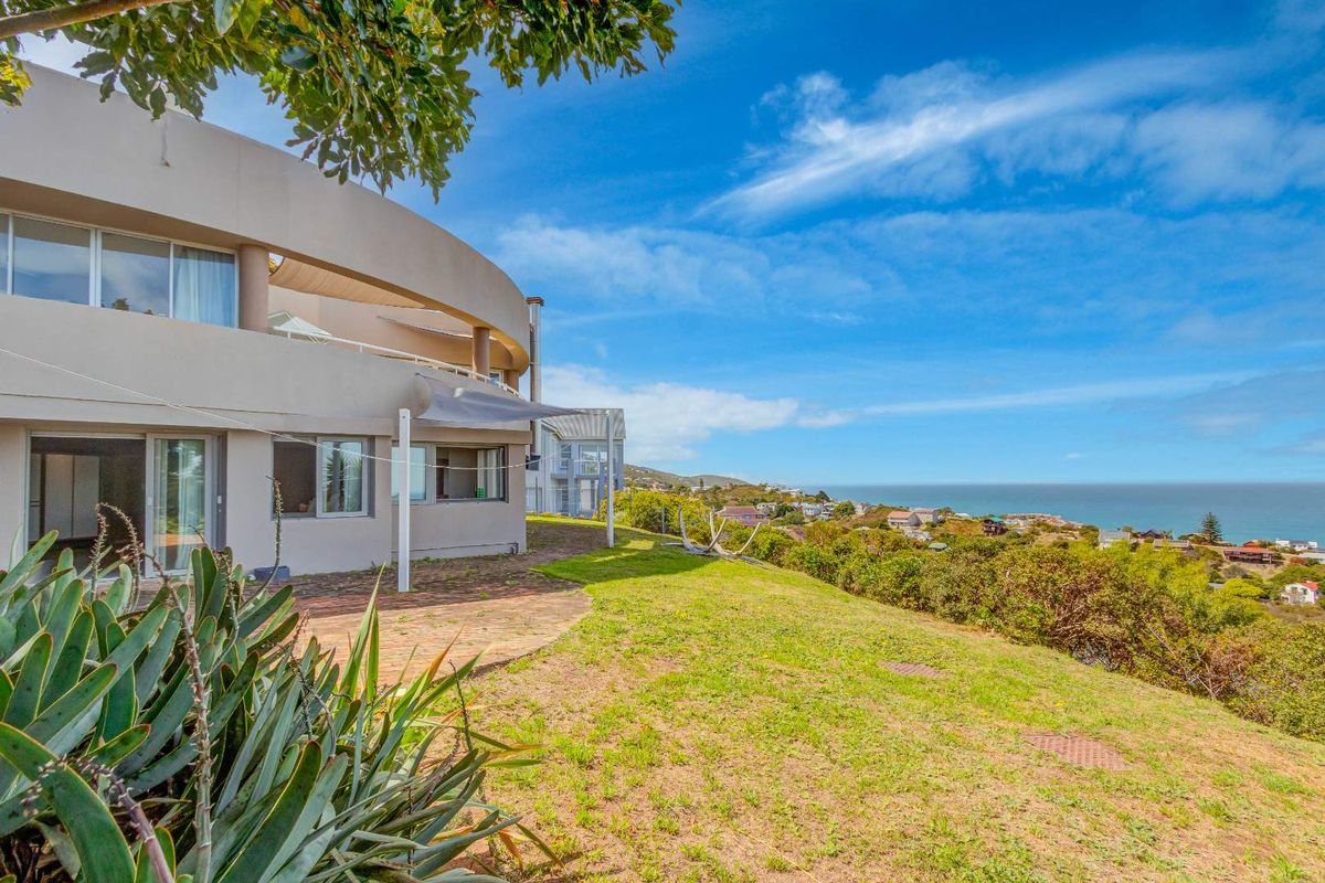 Rear view of the property featuring a curved architectural design, paved patio area, and expansive coastal views over the surrounding landscape.