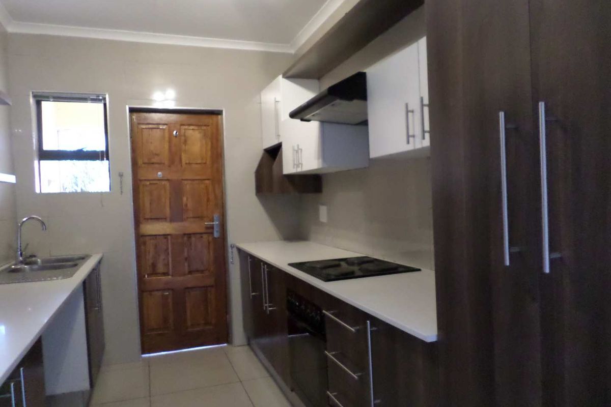 Modern kitchen featuring dark wood cabinetry, white countertops, built-in oven, hob, and extractor fan with tiled flooring.