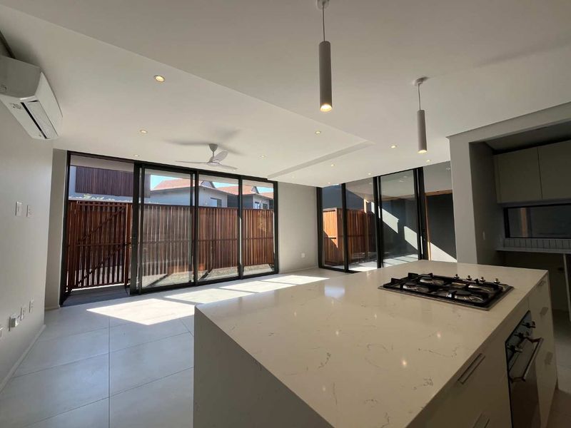 Modern open-plan living and kitchen area featuring a large stone-topped island with integrated gas hob, sleek cabinetry, and expansive sliding doors leading to the exterior.