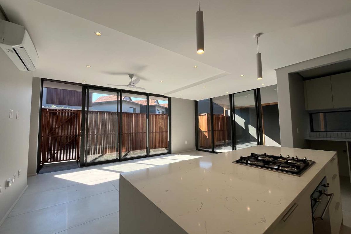 Modern open-plan living and kitchen area featuring a large stone-topped island with integrated gas hob, sleek cabinetry, and expansive sliding doors leading to the exterior.
