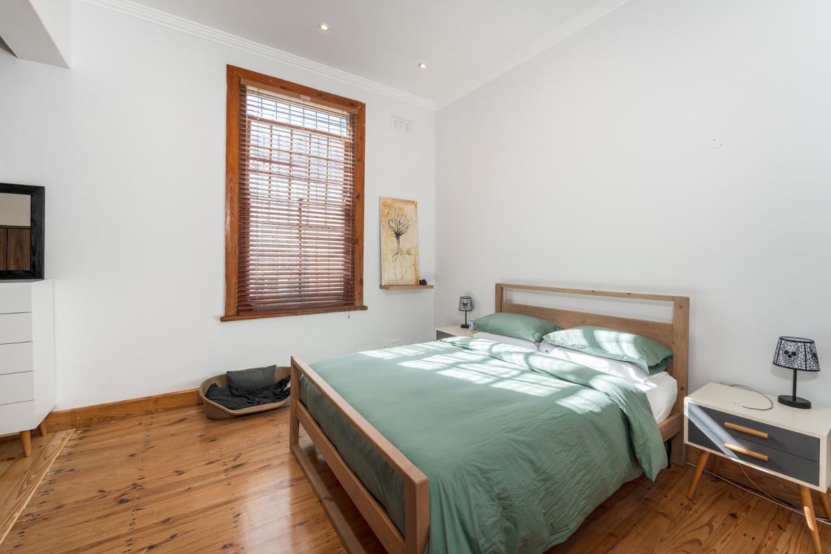 A bright bedroom featuring polished timber flooring, a large window with timber frames and venetian blinds, and recessed ceiling lighting.
