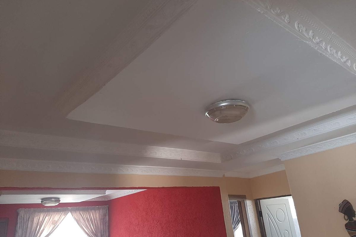 Interior view of a living area featuring decorative ceiling cornices, recessed ceiling detail, and flush-mount lighting fixtures.