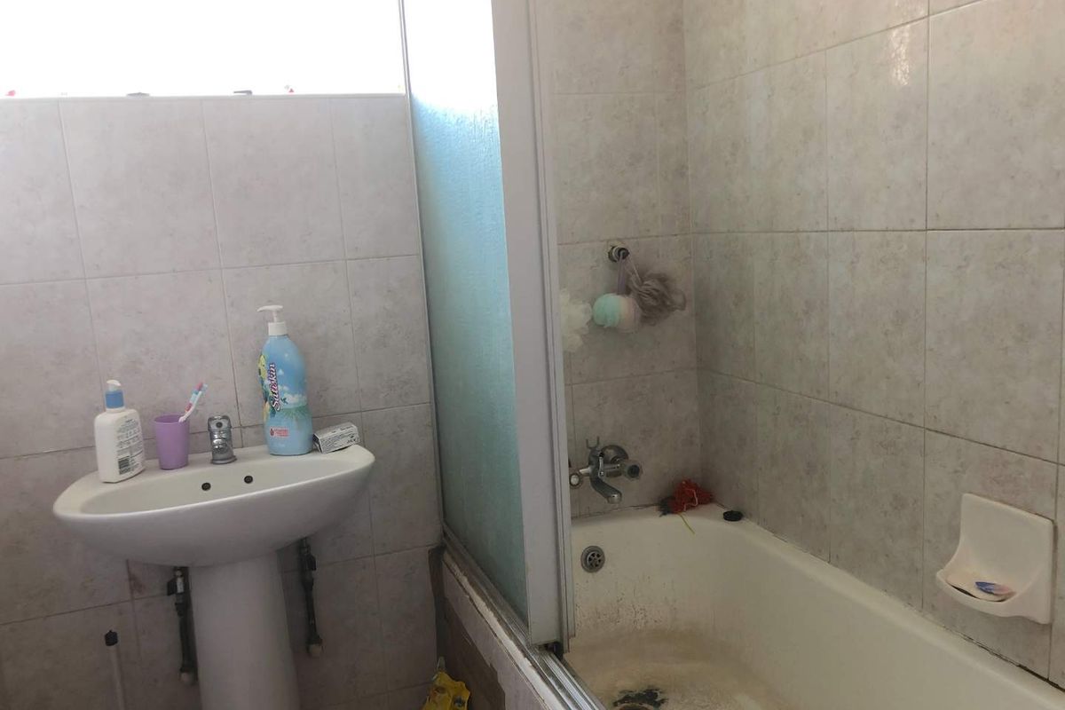 A dated bathroom featuring a pedestal sink, a tiled shower-over-bath combination, and neutral wall tiling.