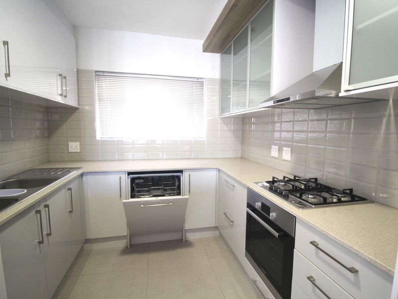 Modern kitchen featuring stone countertops, gas hob, built-in oven, extractor fan, integrated dishwasher, and ample storage cabinetry with a tiled backsplash.