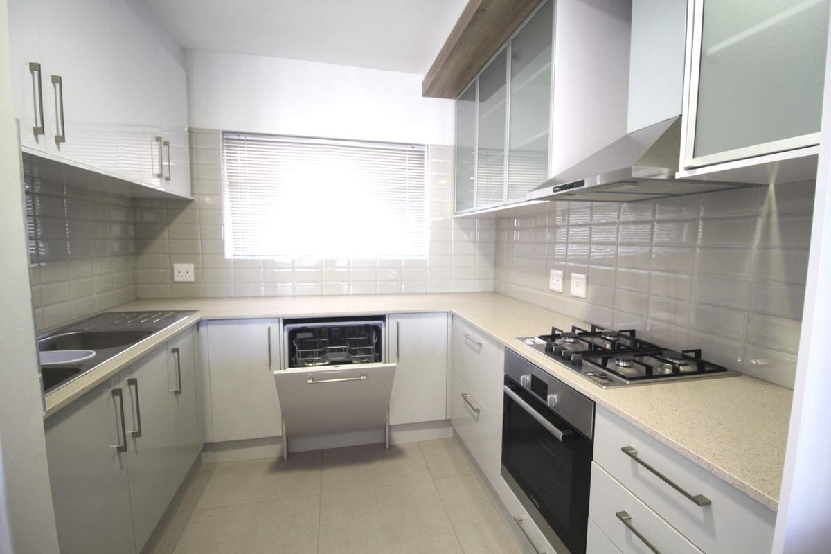 Modern kitchen featuring stone countertops, gas hob, built-in oven, extractor fan, integrated dishwasher, and ample storage cabinetry with a tiled backsplash.