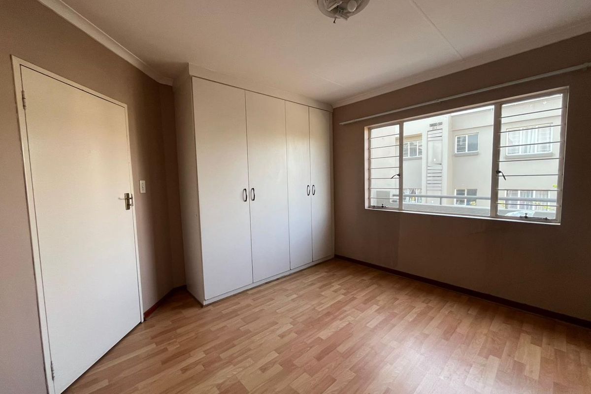 A bedroom featuring built-in cupboards, laminate flooring, and a window with security bars, offering a functional and neutral living space.
