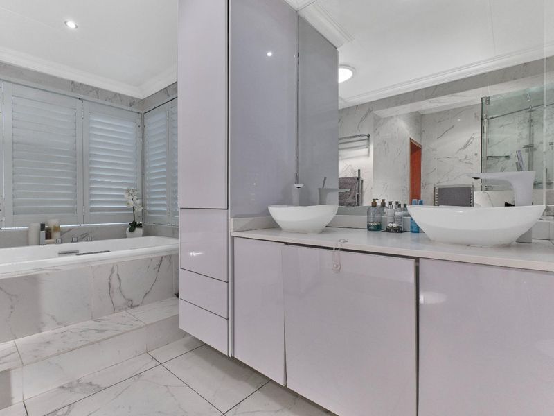 Modern bathroom featuring a double vanity with vessel sinks, built-in cabinetry, a marble-tiled bathtub, and plantation shutters for a clean, luxurious aesthetic.