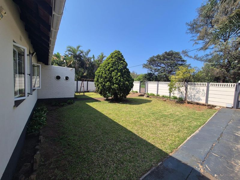 A well-maintained rear garden featuring a manicured lawn, established tree, and secure precast concrete boundary walling.