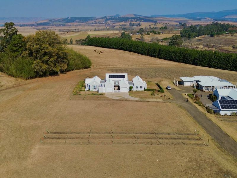 Aerial view of a residential property featuring multiple buildings, solar panel installations, and expansive surrounding land in a rural setting.