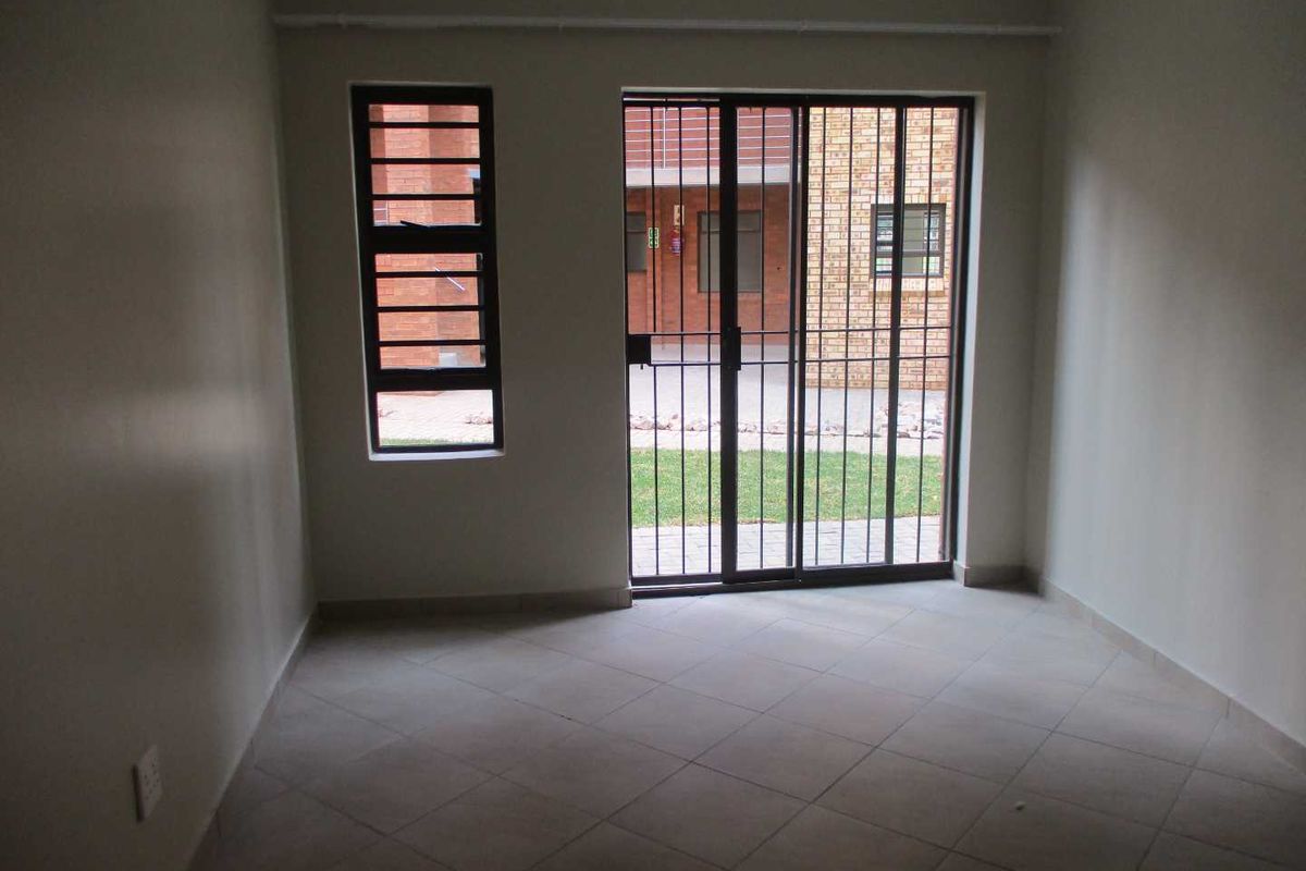 An empty living room featuring tiled flooring, a sliding glass door with security gate, and a window with security bars.