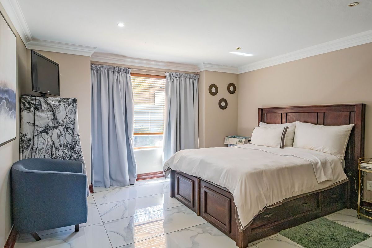 A well-maintained bedroom featuring polished marble-look floor tiles, recessed downlighting, and crown molding, providing a clean and modern aesthetic.