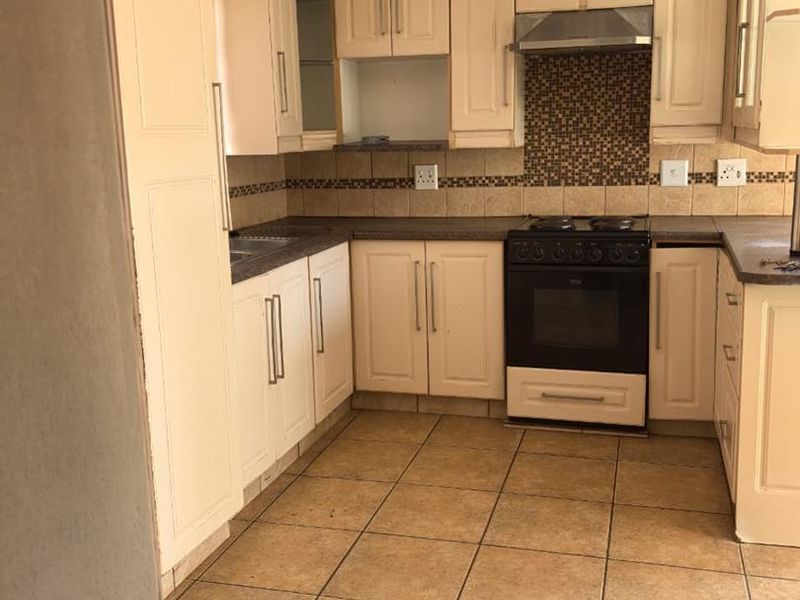A functional kitchen featuring cream-colored cabinetry, tiled flooring, a tiled backsplash, and a built-in oven with an extractor fan.