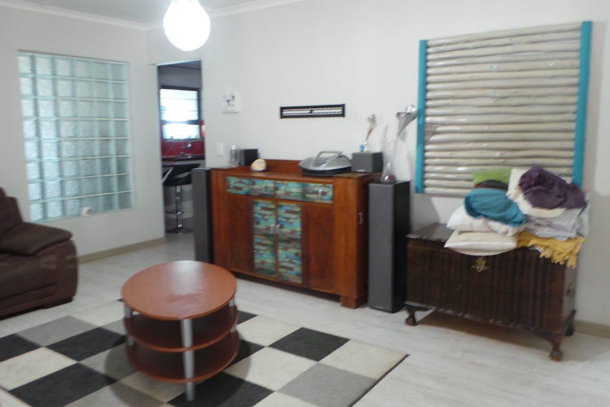 A living room featuring light-toned flooring, a glass block feature wall, and a doorway leading to the kitchen area.