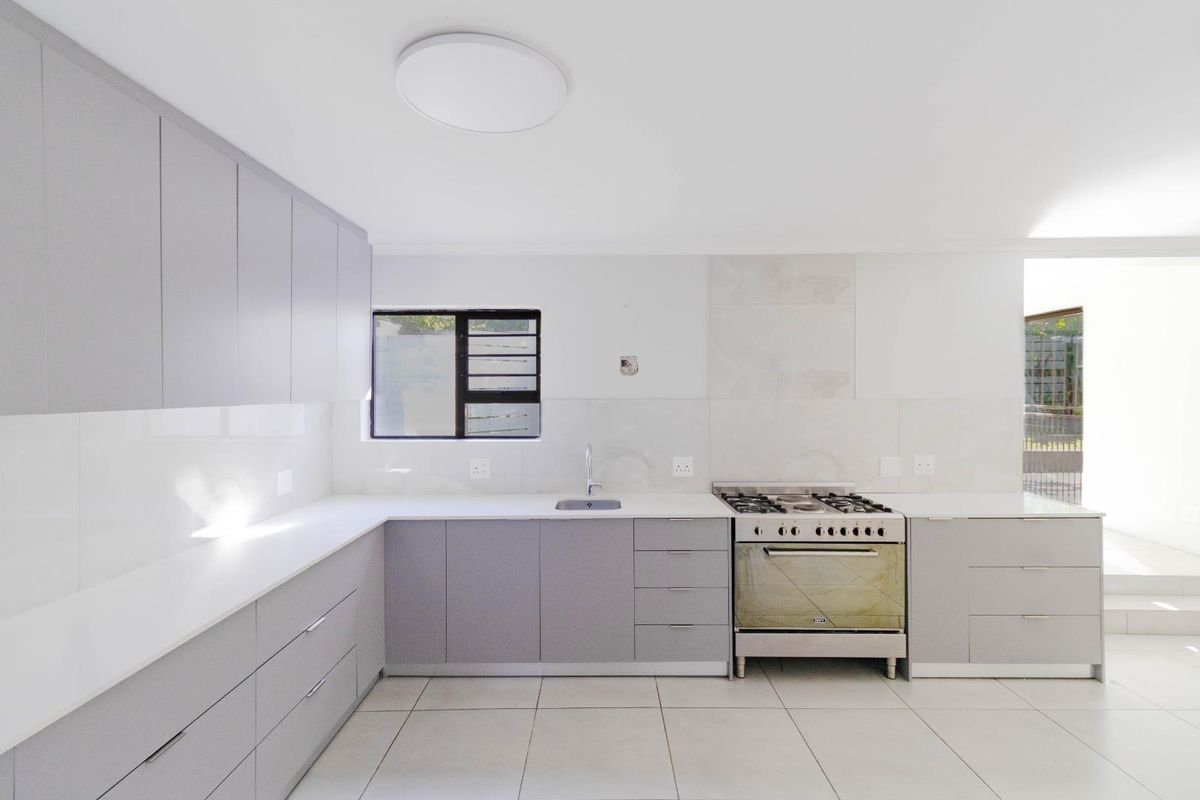 Modern, minimalist kitchen featuring light grey cabinetry, white countertops, a gas stove with oven, and neutral tiled flooring in a clean, open layout.