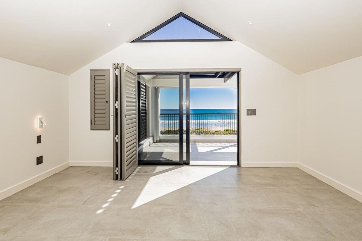 Bright, modern living space featuring large bi-fold doors opening to a balcony with ocean views, complemented by a striking triangular clerestory window.