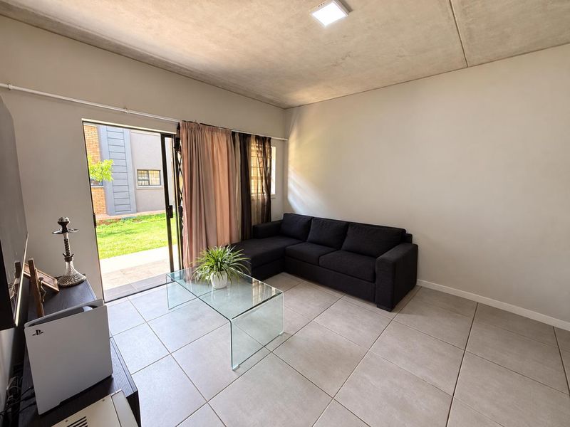 A bright living room featuring large format floor tiles, an exposed concrete ceiling, and a sliding glass door providing direct access to the garden.
