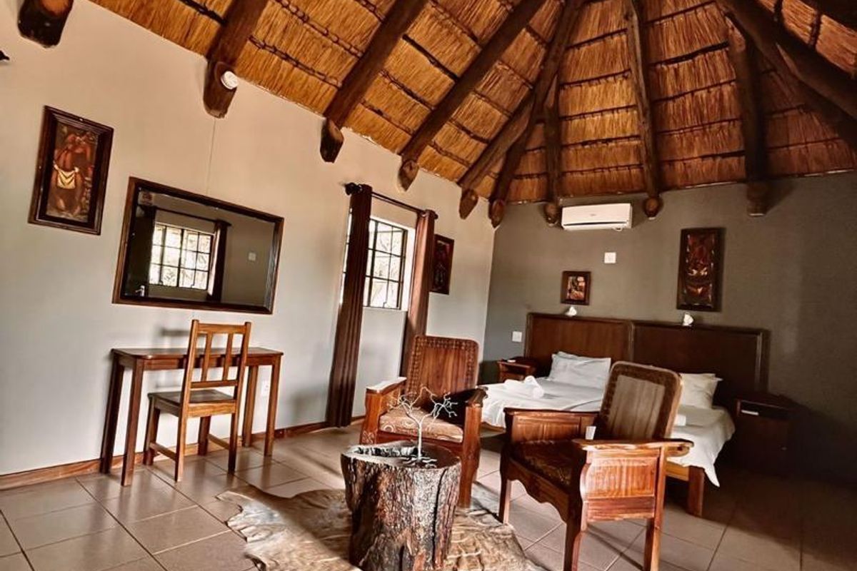 A rustic hotel bedroom featuring a high vaulted thatched roof with exposed timber beams, tiled flooring, and an integrated air conditioning unit.