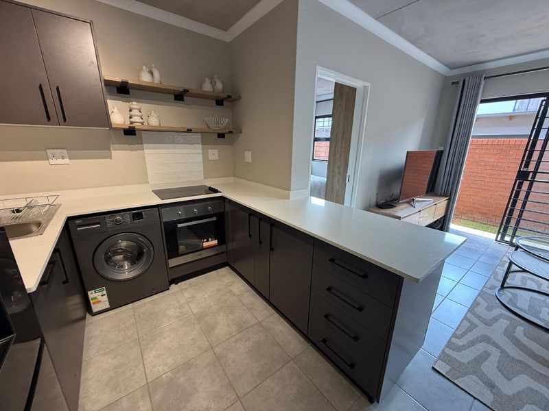Modern open-plan kitchen featuring sleek dark cabinetry, stone countertops, integrated appliances, and tiled flooring, seamlessly flowing into the living area.